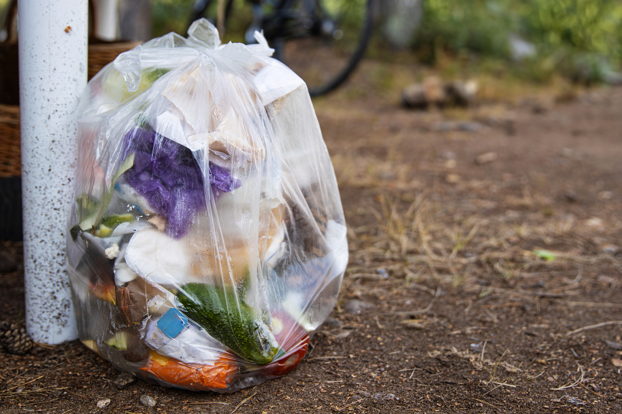 A transparent plastic trash bag full of mixed waste sits on the ground